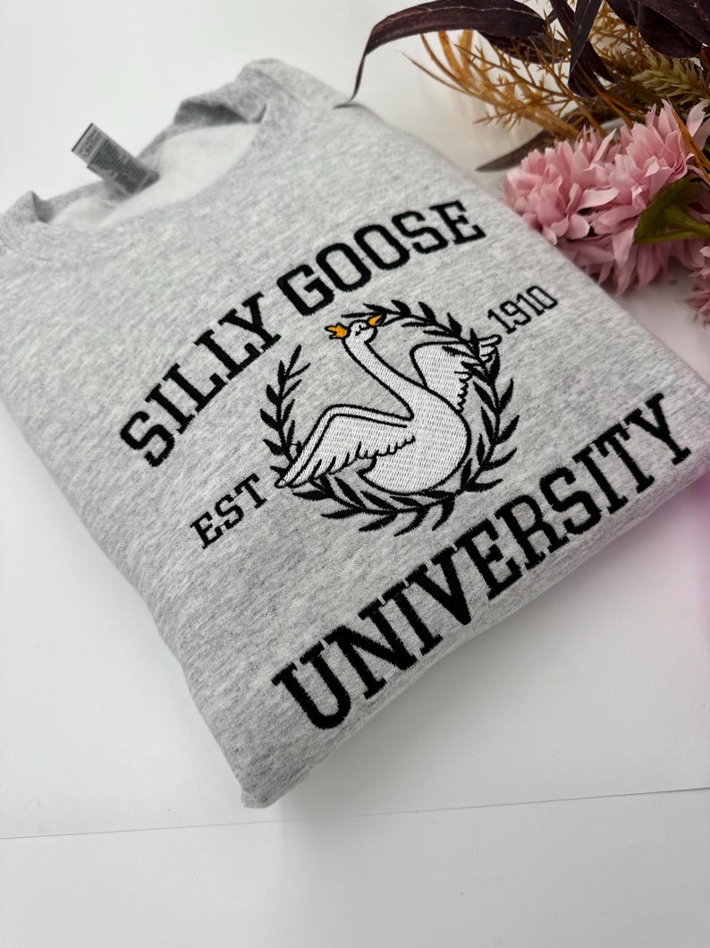 May include: Gray sweatshirt with black embroidered text that reads "Silly Goose University Est. 1910" and a white swan with a gold crown.