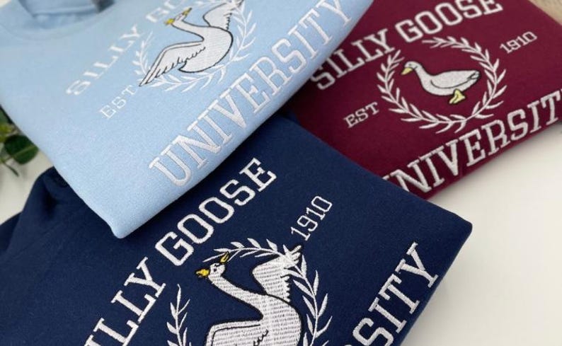 May include: Three sweatshirts with different colored backgrounds and white embroidered text. The text reads "Silly Goose University" and includes a goose graphic. The sweatshirts are blue, maroon, and navy blue.