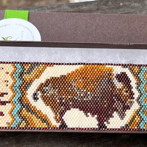 May include: A beaded bracelet with a brown and white bison design, turquoise accents, and a brown metal clasp with a swirl design. The bracelet is in a brown box with white tissue paper.
