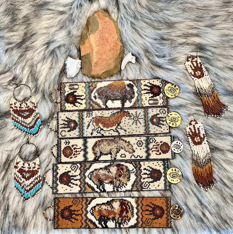 May include: Five beaded bracelets with Native American designs. Each bracelet features a different animal, including a buffalo, a horse, a bear, and two more buffalo. The bracelets are all beige with brown, blue, and white accents. The bracelets are displayed on a white faux fur background with two beaded earrings.