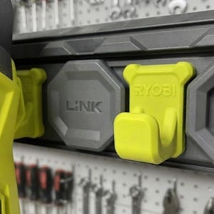 Può includere: Un gancio Ryobi Link verde lime fissato a una guida di stoccaggio a parete grigio scuro. La guida presenta un emblema Link grigio ottagonale e un gancio rettangolare verde lime con il marchio Ryobi in rilievo sulla superficie anteriore.