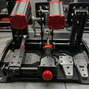May include: A black and silver racing simulator pedal set with red accents. The set includes two pedals with silver cylinders and red tops, a silver footrest, and a black base. The pedals are connected by springs and metal rods.