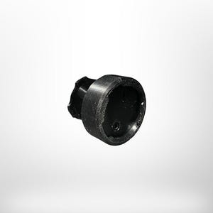 Op de afbeelding: Een zwarte flesstopper met een getextureerd, cilindrisch ontwerp. De stopper heeft een cirkelvormige bovenkant met een klein gaatje en een gegolfde rand aan de tegenovergestelde kant. Het object staat tegen een witte achtergrond.