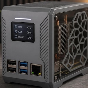 Könnte beinhalten: Ein kompaktes graues Computergehäuse mit einem digitalen Frontdisplay, das CPU 42°C, RAM 38% und USAGE 12% anzeigt. Die Vorderseite verfügt über zwei USB-Anschlüsse, zwei blaue USB-Anschlüsse und einen Ethernet-Port. Die Seitenwand hat ein geometrisches Ausschnittdesign.