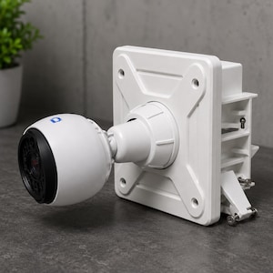 May include: A white security camera with a spherical housing and a black lens, attached to a square mounting bracket. The camera features a small blue indicator light on the top. The mounting plate has four circular screw holes and a mechanical arm.