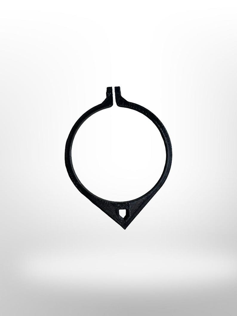 May include: A black, circular object with a teardrop-shaped bottom and a small, shield-like cutout. The top of the circle is split. The object is set against a white background.