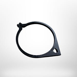 May include: A black, 3D-printed, circular object with a teardrop-shaped extension. The object has a textured surface and a small triangular cutout. The design appears to be a clamp or fastener.
