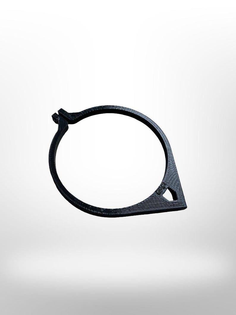 May include: A black, 3D-printed, circular object with a teardrop-shaped extension. The object has a textured surface and a small triangular cutout. The design appears to be a clamp or fastener.