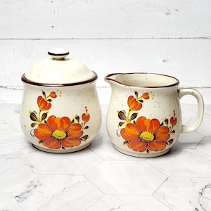 May include: A vintage ceramic sugar and creamer set with a white background and orange and brown floral design.