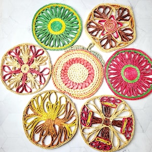 May include: Set of seven woven trivets in various colours and patterns. The trivets are round and feature a variety of geometric and floral designs. The trivets are made of natural materials and have a rustic, handmade look.