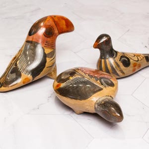 May include: Three hand-painted ceramic bird figurines. The birds are in various poses and feature black, white, orange, and brown paint.
