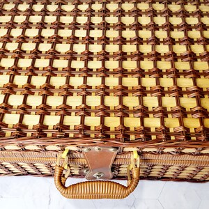 May include: A woven picnic basket with a brown leather handle and clasp. The basket is made of light and dark brown woven material. The handle is curved and attached to the basket with metal hardware.