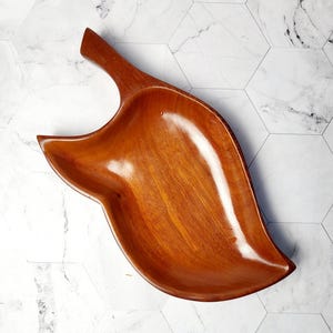 Peut inclure: Un grand bol de service en bois en forme de feuille. Le bol est en bois brun foncé et a une finition lisse et polie.