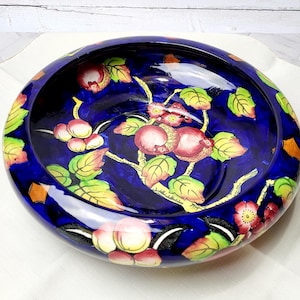 May include: A blue ceramic bowl with a floral design. The bowl features a stylized tree with yellow and green leaves and pink and red flowers. The bowl is decorated with a glossy glaze.