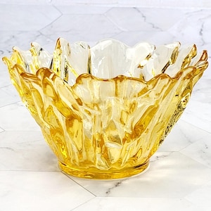 May include: A yellow glass bowl with a textured, wavy design. The bowl is made of clear glass with a yellow tint.