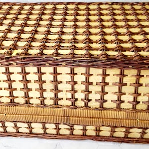 May include: A rectangular picnic basket with a woven design. The basket is made of light brown and dark brown wicker, with a lid and a rectangular shape. The weave pattern is intricate and detailed.