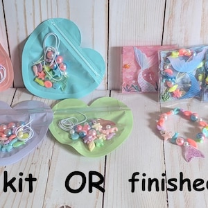 May include: DIY bracelet kits and finished bracelets are displayed. The kits are in heart-shaped bags with beads and elastic. Finished bracelets with mermaid tail charms are also shown. Text reads "DIY kit OR finished bracelet."