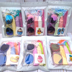 May include: Six clear plastic bags each containing sunglasses, a pop-it toy, lip balm, and other summer-themed accessories. Each bag has a different sticker, including a cupcake, pineapple, and flip-flops.
