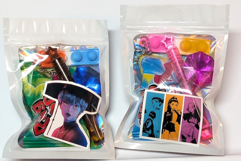 May include: Two clear plastic bags filled with colorful items. One bag contains a sticker of a person with blue skin and a black hat, a blue pop-it, and a star-shaped keychain. The other bag has a sticker with three women, a pink pop-it, and a pink star-shaped pen.