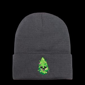 May include: A dark gray beanie with a green cartoon marijuana leaf embroidered on the front. The leaf has a smiling face with black eyes and a pink mouth.