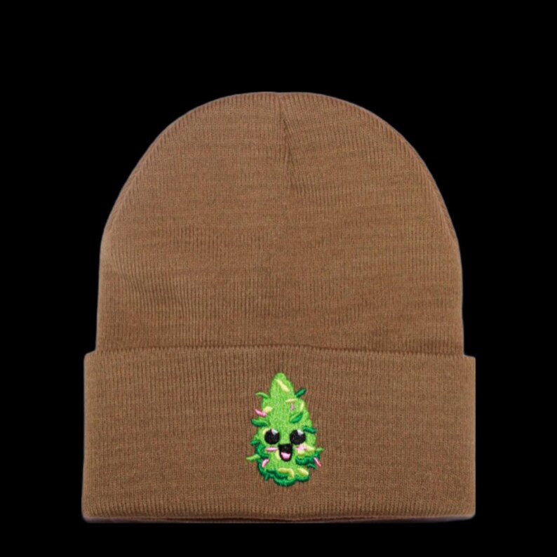 May include: A brown beanie with a green and white embroidered cartoon marijuana leaf with a smiling face.