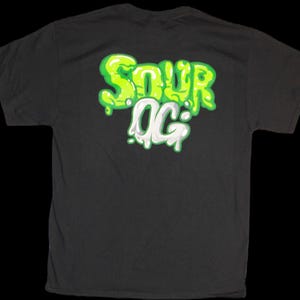 May include: Black t-shirt with a green and white graphic that says "Sour OG" in a dripping font.