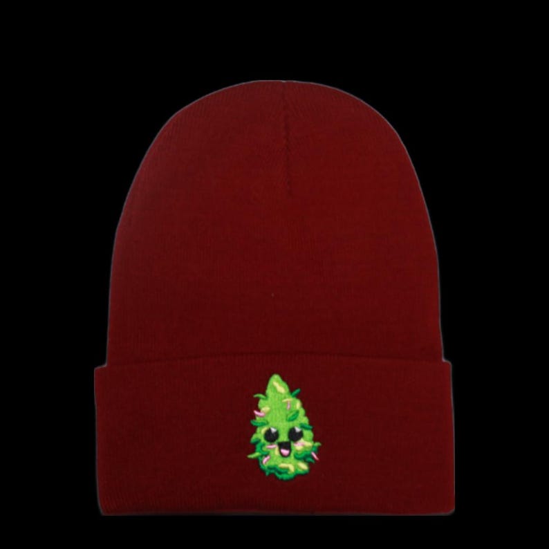May include: A red beanie with a green cartoon marijuana leaf embroidered on the front. The leaf has a smiling face.
