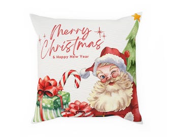 Puede incluir: Cojín cuadrado blanco con una ilustración de acuarela de Papá Noel guiñando un ojo. El diseño incluye un árbol de Navidad, regalos envueltos con lazos rojos y un bastón de caramelo. El texto "Merry Christmas & Happy New Year" está escrito en rojo.