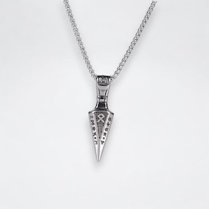 May include: A silver necklace with a pendant shaped like a spearhead. The spearhead is engraved with runes and a symbol.