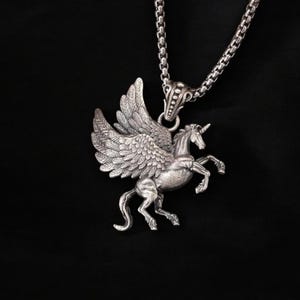May include: Silver pendant necklace featuring a detailed winged unicorn design. The pendant is attached to a silver chain.