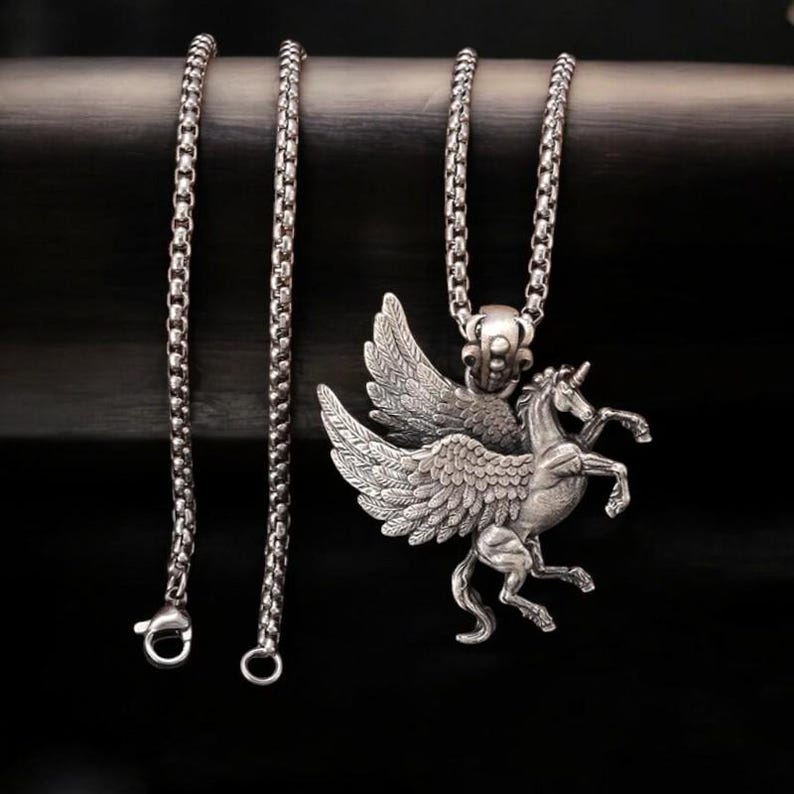 May include: Silver chain necklace featuring a winged unicorn pendant. The pendant is detailed with intricate wings and a horse head.