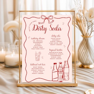 May include: A framed sign with a pink background and red text. The sign reads "Build Your Own Dirty Soda" and lists soda recipes like "Raspberry Dream" and "Dirty Cola." Decorative elements include a bow and illustrations of bottles.