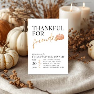 Op de afbeelding: Een Friendsgiving-dineruitnodiging met de woorden "THANKFUL FOR friends" in zwart en goud. De uitnodiging bevat een pompoenillustratie en details voor het evenement, omringd door pompoenen, kaarsen en herfstbladeren.