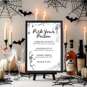 May include: A Halloween-themed sign with the text "Pick Your Poison" lists cocktail options. The black framed sign is on a small easel, surrounded by candles, pumpkins, and spiderwebs. Two bottles of liquor are visible.
