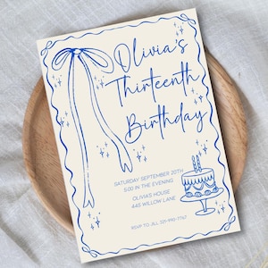 Op de afbeelding: Een cr&egrave;me verjaardagskaart met blauwe accenten. De tekst "Olivia's Thirteenth Birthday" is in een sierlijke lettertype geschreven. De kaart bevat datum, tijd, locatie en een telefoonnummer voor RSVP.