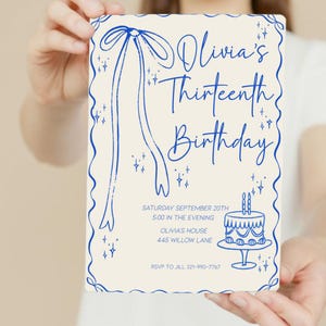 Op de afbeelding: Een cr&egrave;mekleurige verjaardagsuitnodiging met blauwe accenten. De uitnodiging bevat de tekst "Olivia's Thirteenth Birthday" in een scriptlettertype, samen met evenementdetails en een taartillustratie. Een blauwe strik en linten sieren de bovenkant.