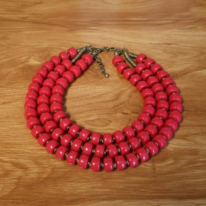 May include: A vibrant pink statement necklace. The necklace features multiple strands of rounded, cylindrical beads. The beads are a bright, solid pink color, strung together with silver-toned metal accents and a matching clasp.