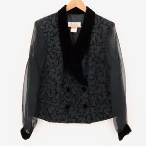 May include: A black blazer featuring a sheer fabric body with a dark velvet scrollwork pattern. The garment has a wide black velvet shawl collar, long sheer sleeves with velvet cuffs, and a double-breasted front closure with two velvet buttons.