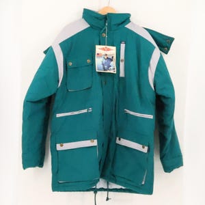 May include: A teal and light gray winter jacket featuring a high collar, a front zipper closure, and multiple pockets with snap buttons. A rectangular product tag with an image of a person wearing the jacket is attached to the collar area.