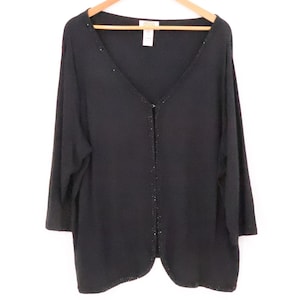 May include: Black cardigan with a V-neck and three-quarter sleeves. The front and neckline are embellished with small, sparkling accents. The garment is hanging on a wooden hanger against a white background.