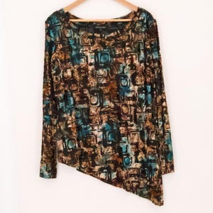 May include: A long-sleeve top featuring an asymmetrical hemline and a round neckline. The garment displays a multi-colored abstract geometric pattern in shades of brown, black, and teal. The brand label reads "WORLD MAX" at the inner neck.