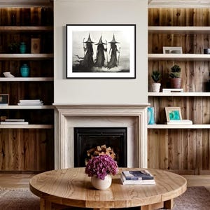 May include: A black and white framed print of three witches wearing pointed hats and long robes, walking in a line. The print is hanging on a wall above a fireplace in a living room.