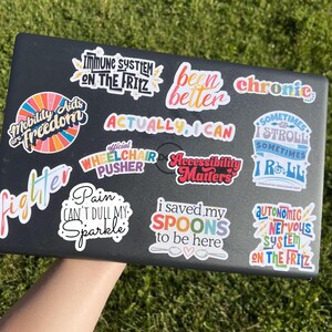 May include: A black laptop covered in colorful stickers with various phrases, including "Mobility Aids are Freedom," "Actually I Can," and "I saved my SPOONS to be here." The stickers have a variety of fonts and designs.