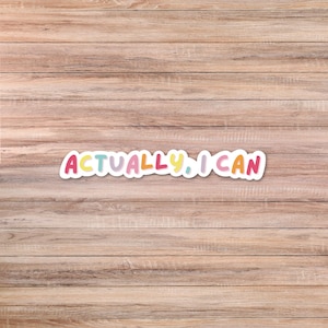May include: A white sticker with the phrase "ACTUALLY, I CAN" in colorful bubble letters. The sticker is set against a wooden background.