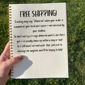 May include: A spiral-bound notebook with lined paper. The cover is not visible. The text "FREE SHIPPING!" is written at the top, followed by a message about order tracking. The notebook is held by a person.