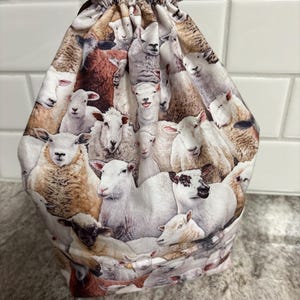 May include: A drawstring bag featuring a repeating pattern of sheep in various colors and poses. The sheep are primarily white, brown, and black, creating a detailed and textured design. The bag's top is gathered with a drawstring closure.
