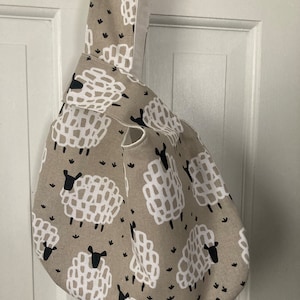 May include: A beige tote bag with a white and black sheep print. The bag has a single handle and is made of a soft, woven fabric.