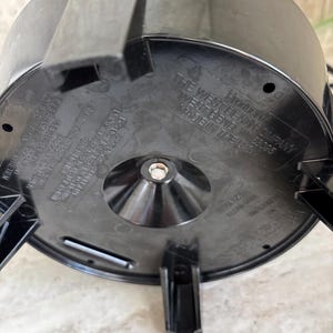 Puede incluir: Base de electrodom&eacute;stico de pl&aacute;stico negro con tres patas y un tornillo central. La base tiene el texto "THE WEST BEND COMPANY" y "MADE IN THE USA" impreso. La base del electrodom&eacute;stico est&aacute; sobre una superficie clara.