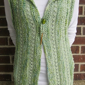 Puede incluir: Un chaleco de punto de ganchillo verde y blanco con cierre de botón. El chaleco tiene cuello y es sin mangas.