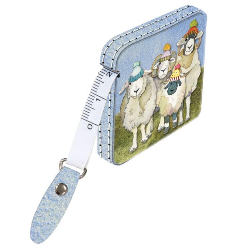 Op de afbeelding: Een blauwe en witte stoffen meetlint met een ontwerp van vier schapen die hoeden dragen. Het meetlint is 15 cm lang en heeft een metalen ring aan het einde.